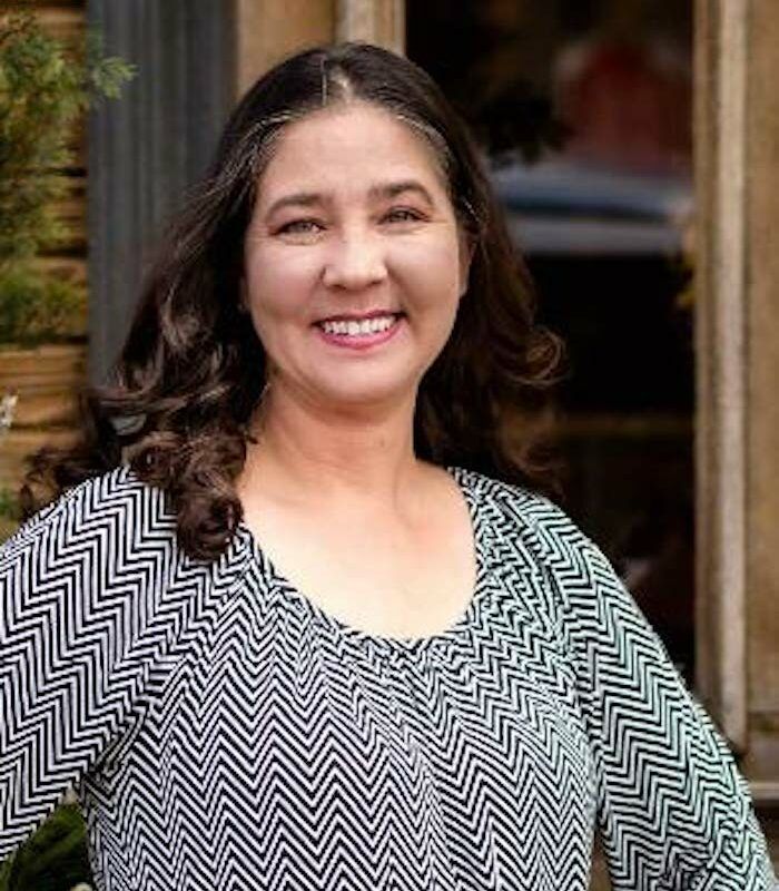 Woman in a business suit with arms crossed, smiling confidently, in a modern office.