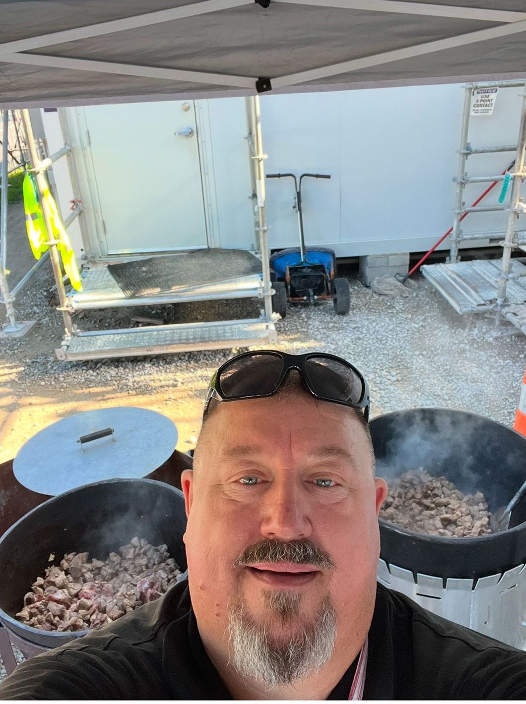 A man with a beard is taking a selfie in front of pots of food.