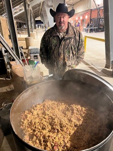 A man in a cowboy hat is standing next to a large pot of food.