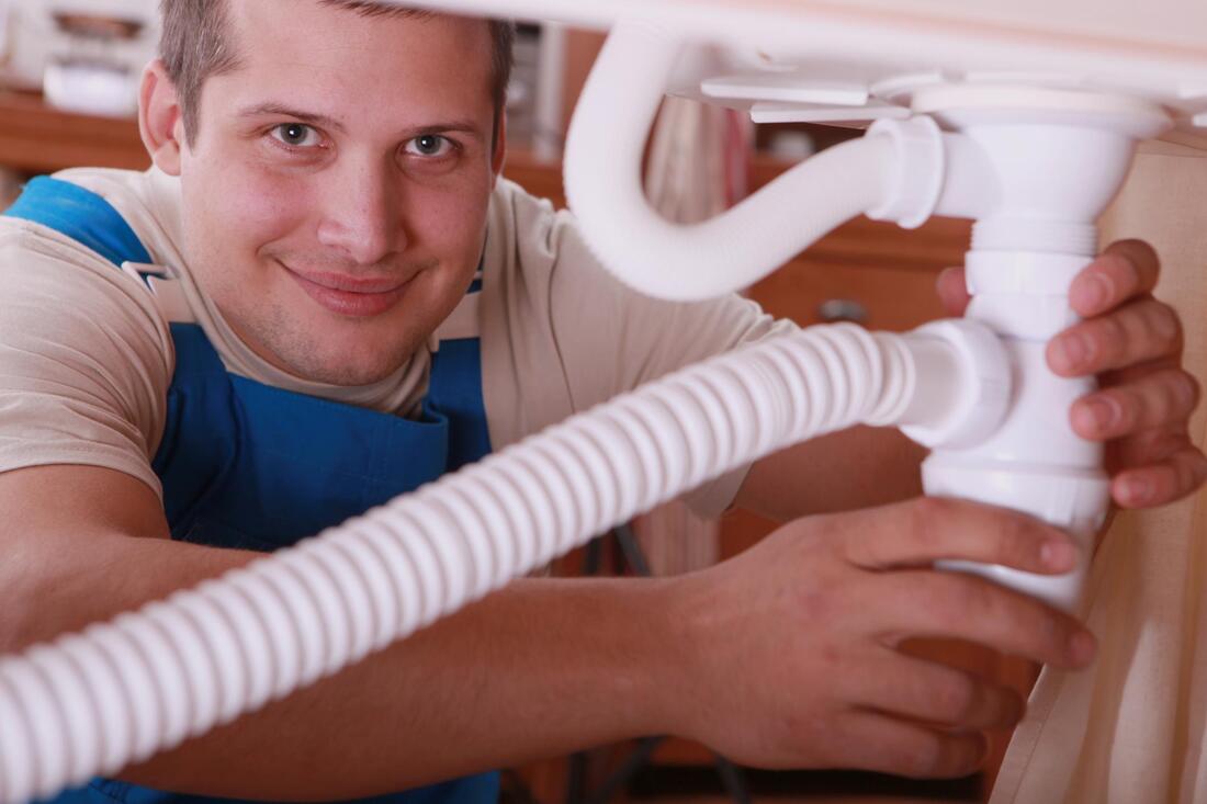 man in his working clothes is fixing the plumbing under a sink