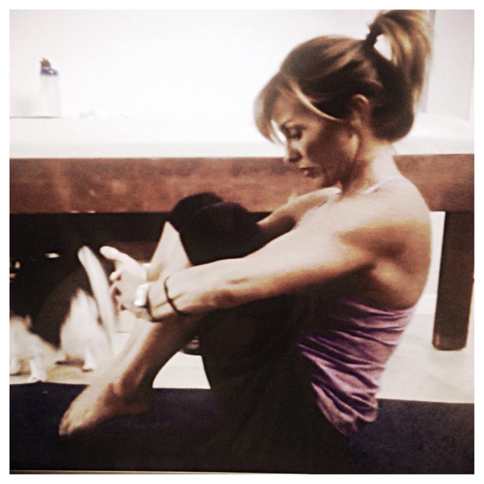 A woman in a purple tank top sits on a yoga mat next to a cat