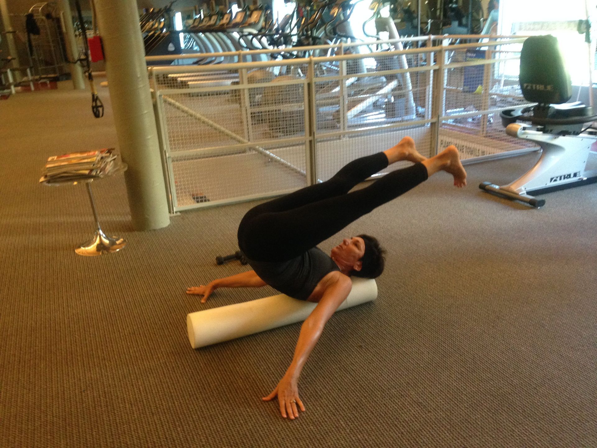 A woman is laying on a foam roller in a gym.