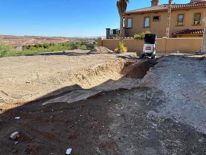 A bulldozer is digging a hole in the dirt in front of a house