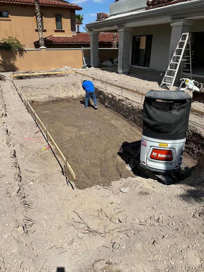 A man is digging a hole in the dirt in front of a house.