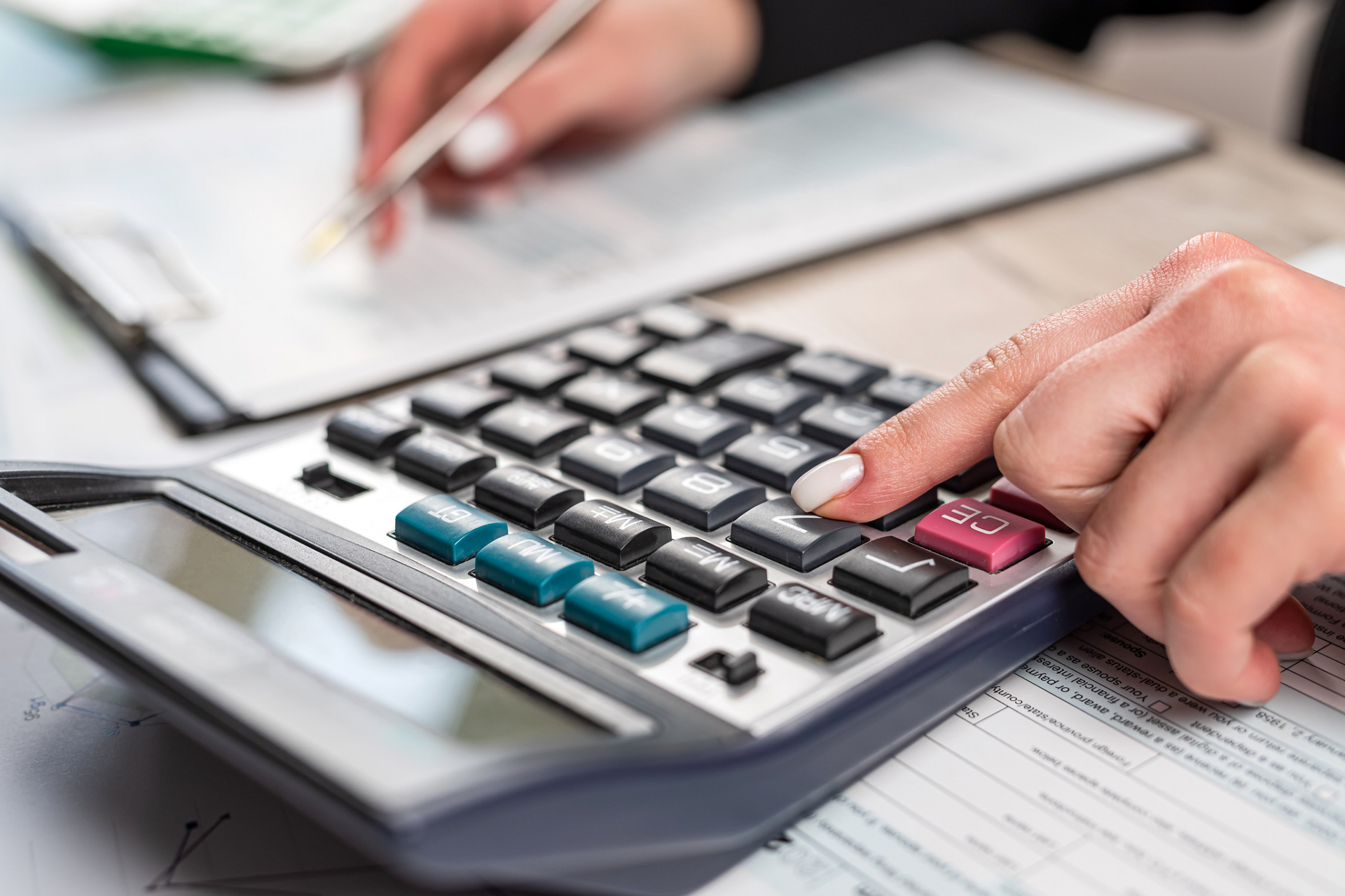 A woman is using a calculator and writing on a piece of paper.