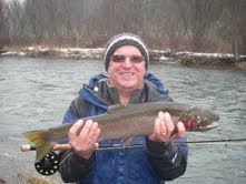 A man is holding a rainbow trout in his hands in front of a river.