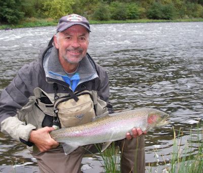 A man is holding a large rainbow trout in front of a river.