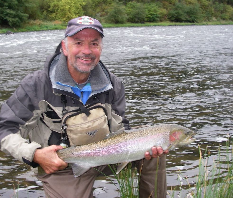 A man holding a rainbow trout in front of a river