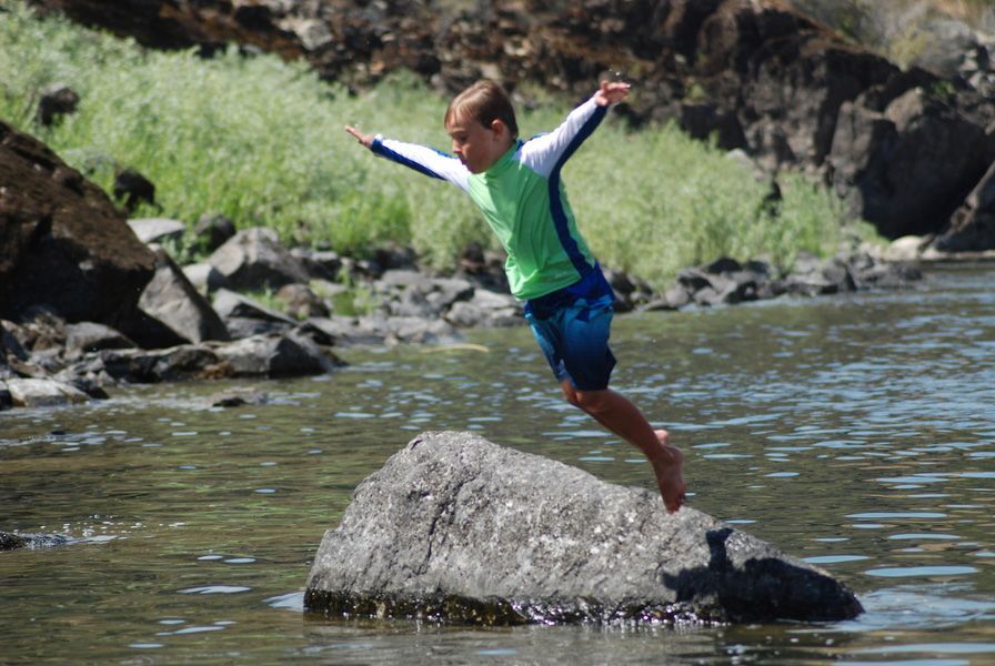 Young Boy Jumping Off a Rock Into a River