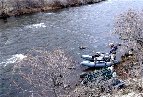 A man is fishing in a river next to a boat.