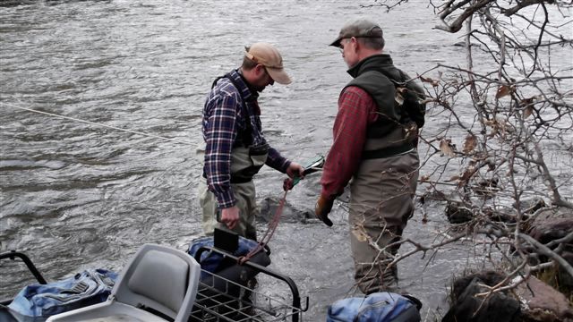 Two men are standing next to a river talking to each other.