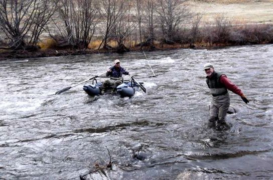 Two men are rowing a boat down a river.