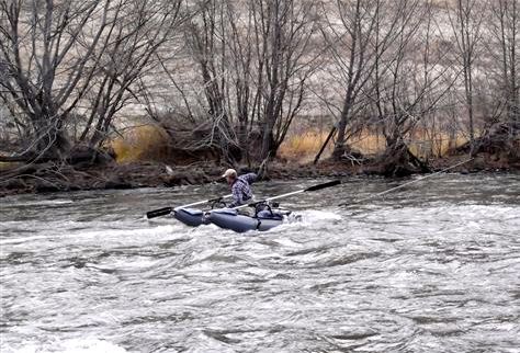 A man is rowing a kayak down a river.