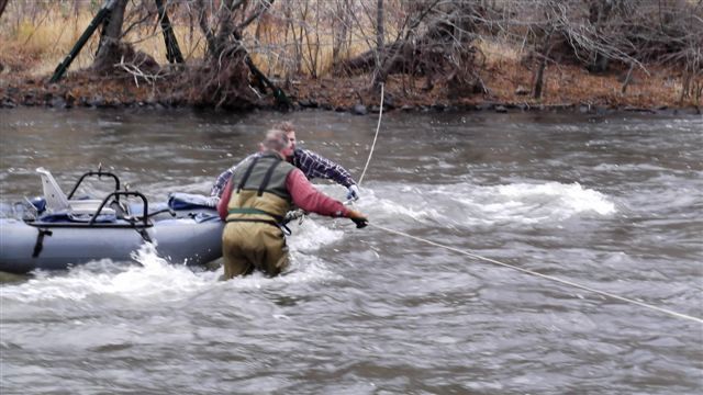 A man is fishing in a river next to a raft.