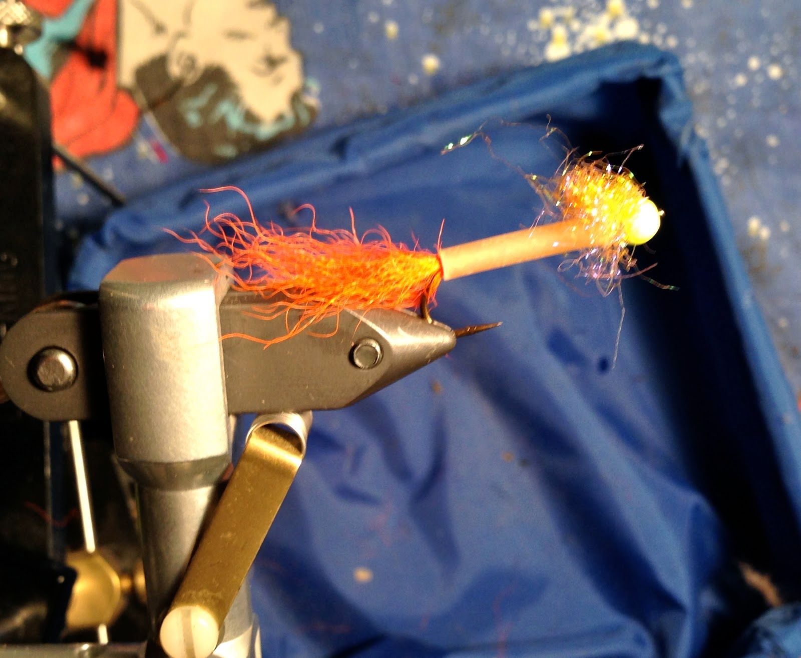 A close up of a fly tying tool with orange yarn