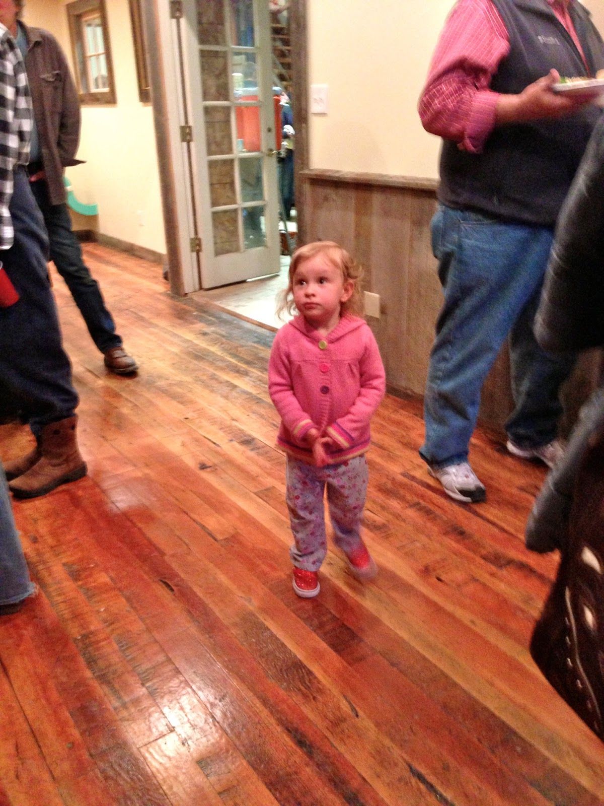 A little girl in a pink jacket is standing on a wooden floor