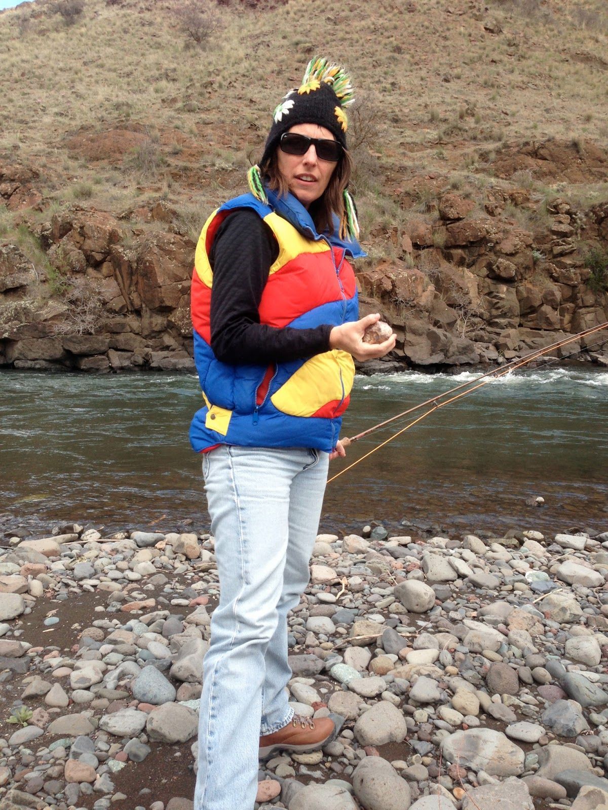 A woman in a colorful vest is fishing by a river