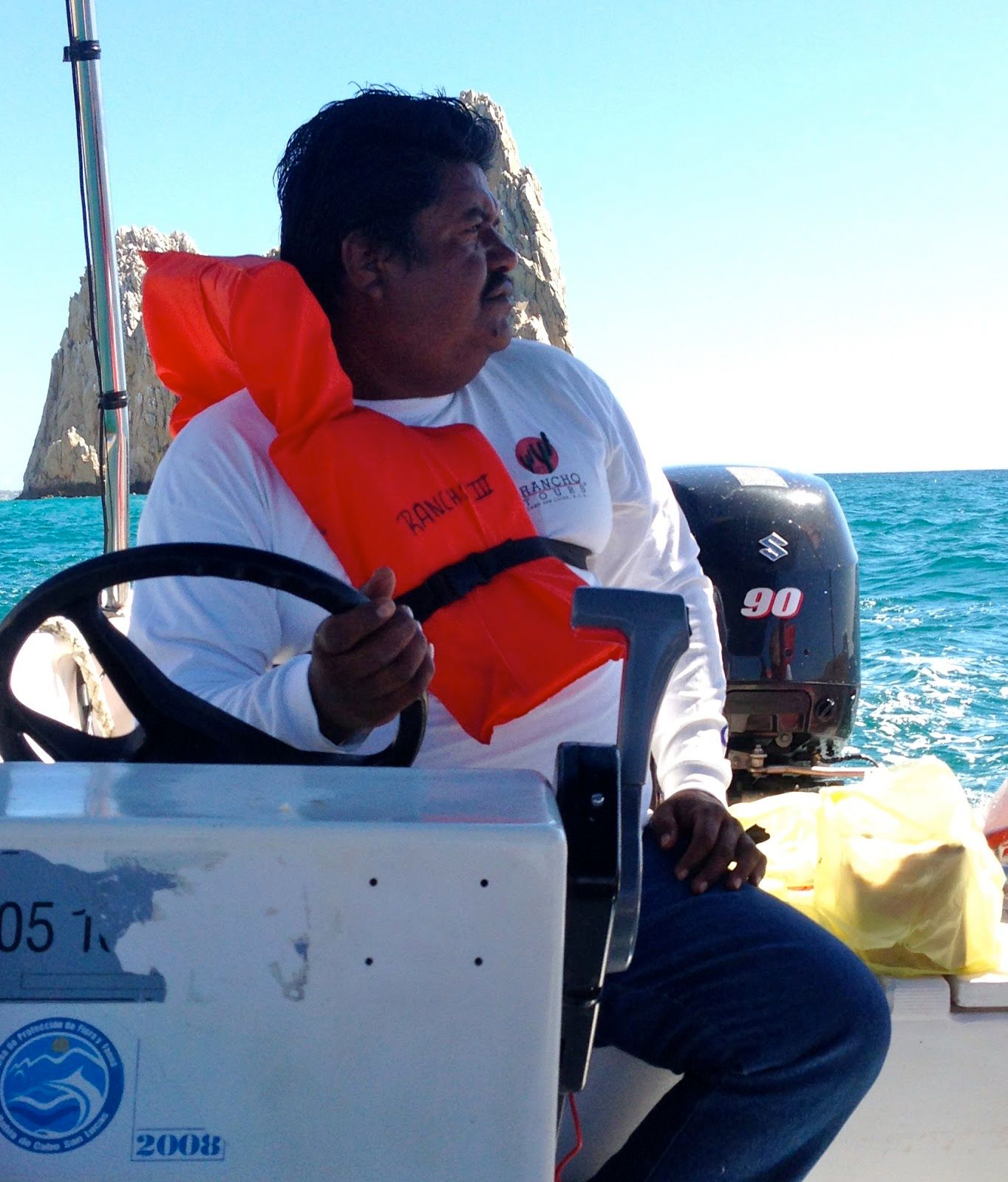 A man wearing an orange life jacket is sitting on a boat