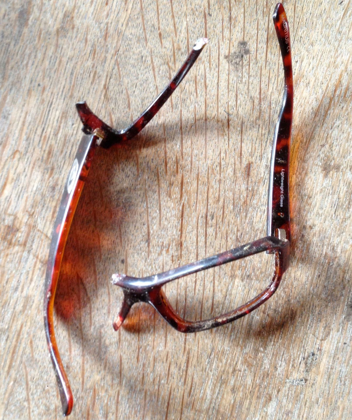 A pair of broken glasses is laying on a wooden surface