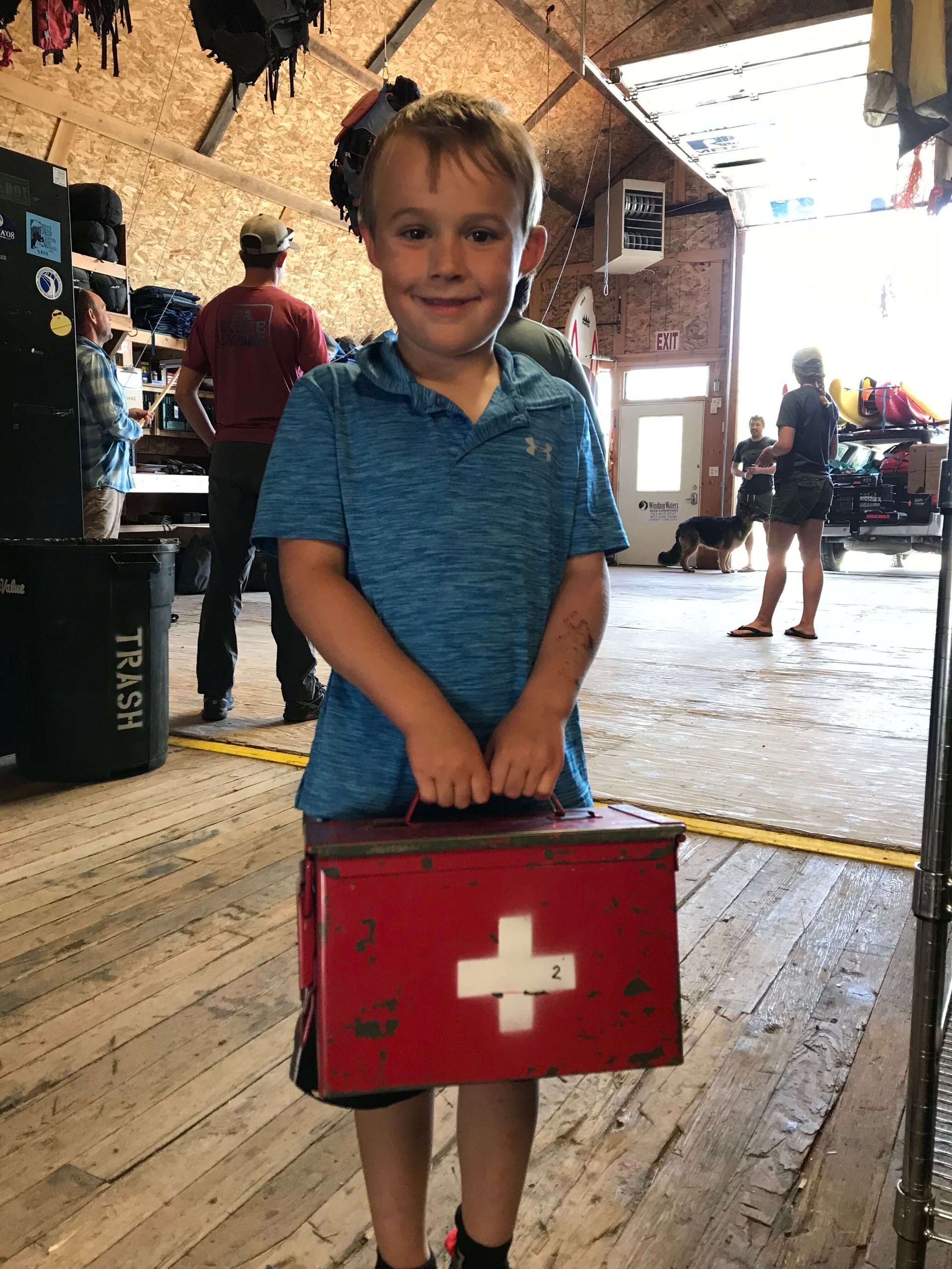 A young boy is holding a red box with a white cross on it.