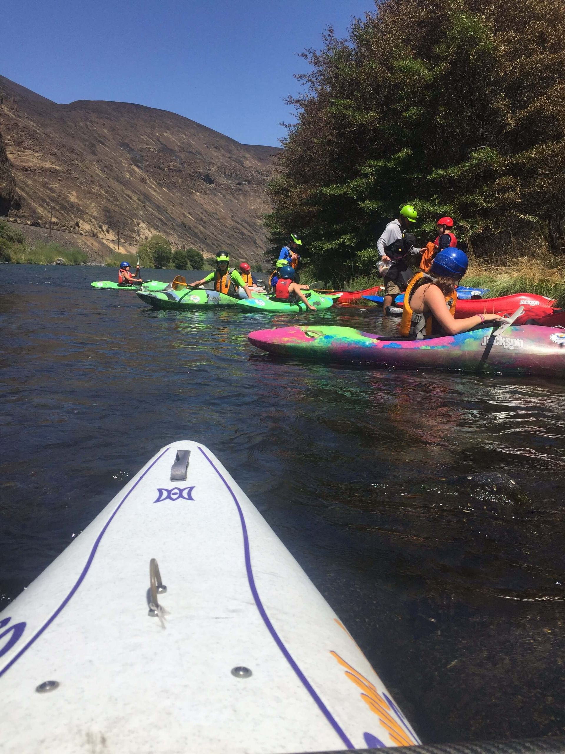 A group of people in kayaks on a river with mountains in the background