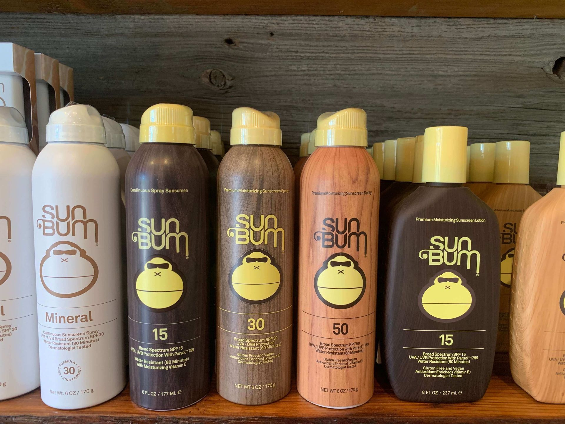 Several bottles of sun bum spray are lined up on a wooden shelf