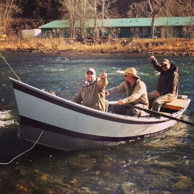 Three Men in A Boat on A River with A Green Building in The Background