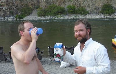 Two men are standing next to each other drinking milk from a carton.