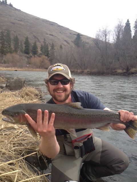 A man is holding a large fish in front of a river