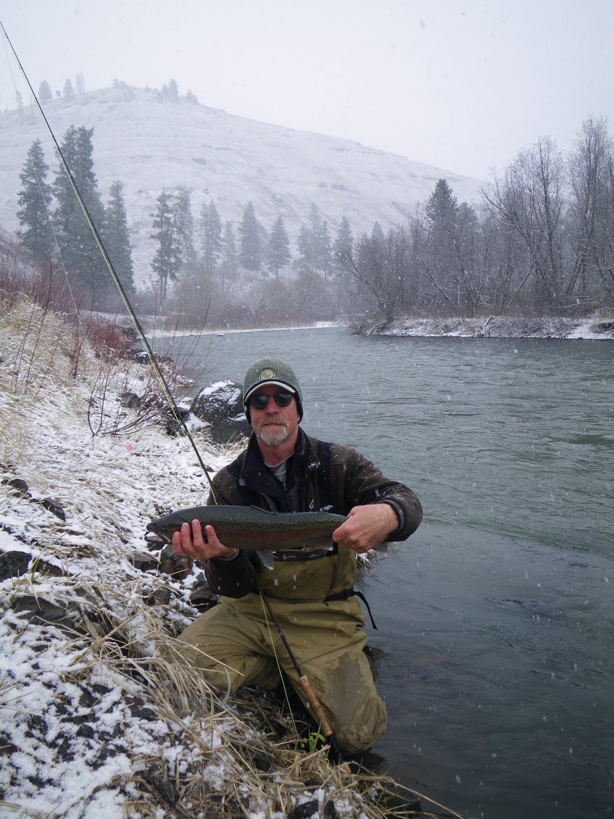 A man is kneeling down in the snow holding a large fish.