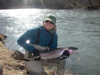 A woman is kneeling down next to a river holding a large fish.