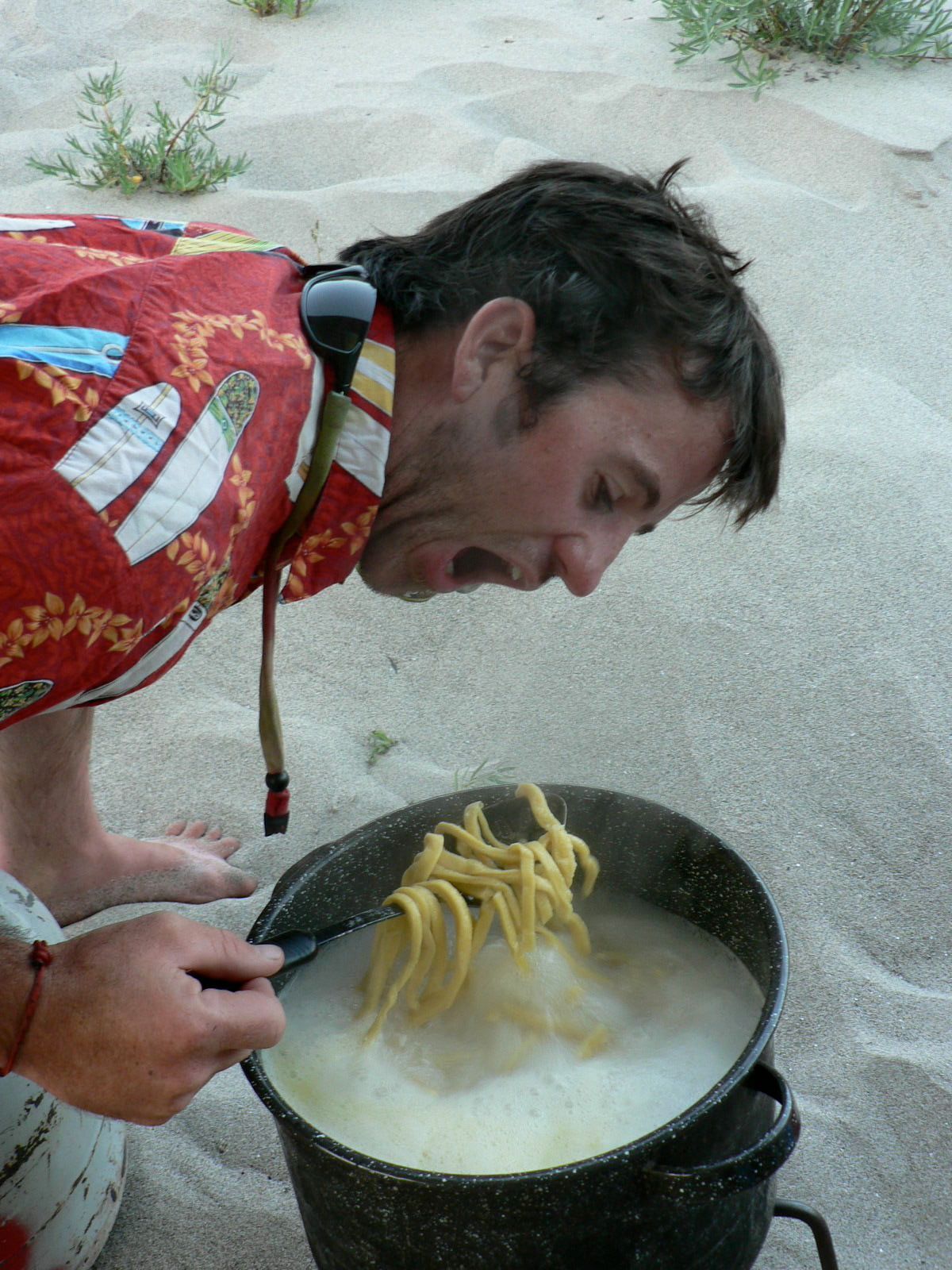 A man in a red shirt is cooking noodles in a pot