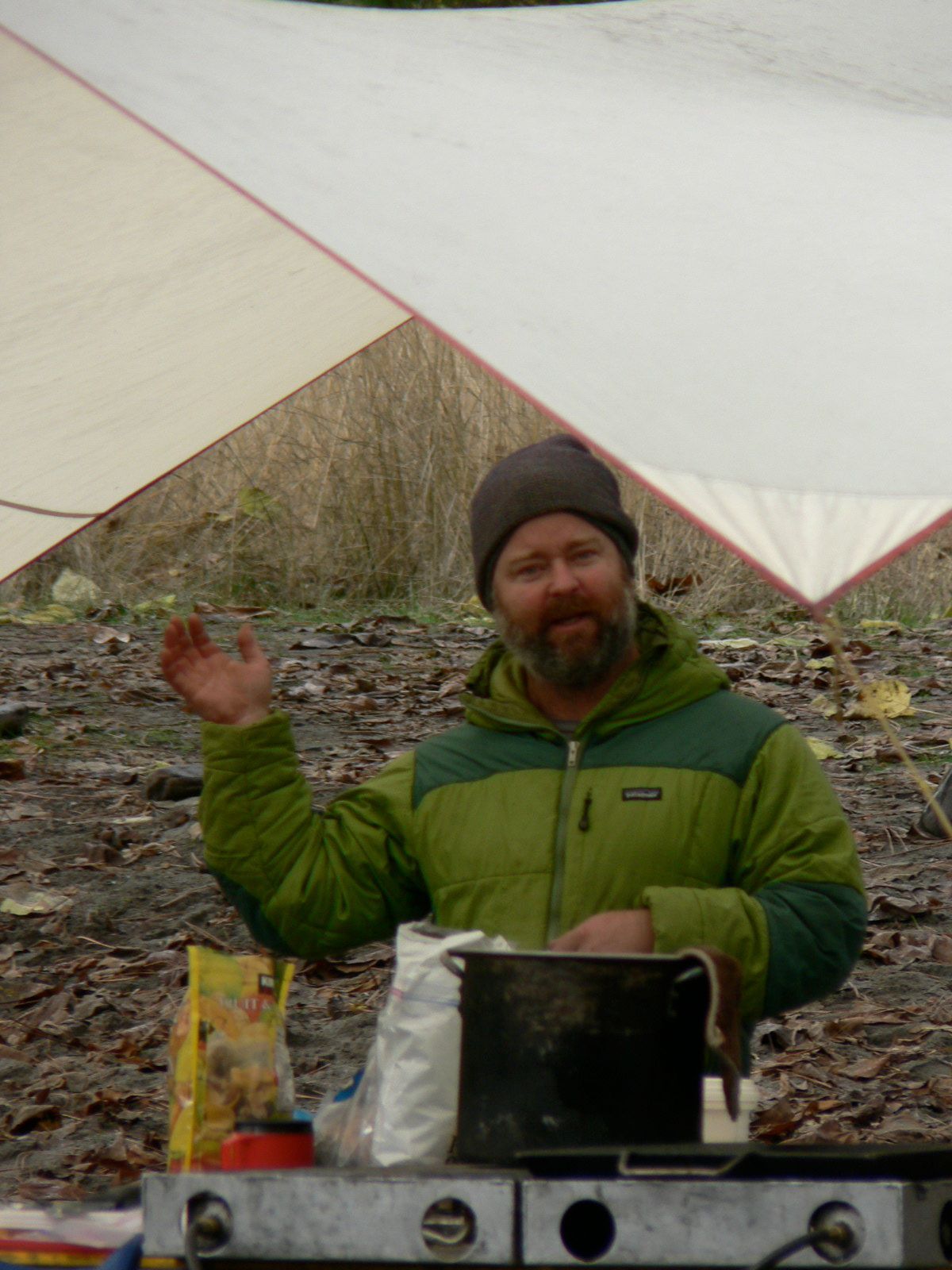 A man in a green jacket is cooking under a white tarp