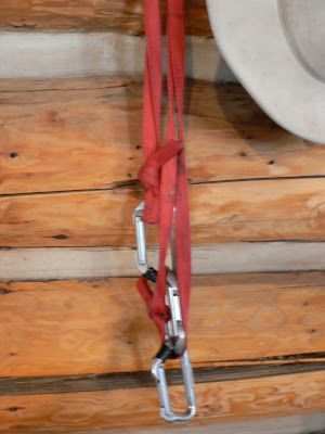 A red rope with carabiners attached to it is hanging on a wooden wall