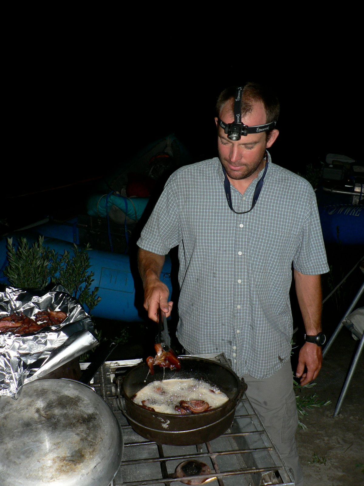 A man wearing a headlamp is cooking food in a frying pan