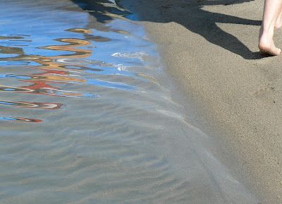 A person is walking barefoot on the beach near the water.