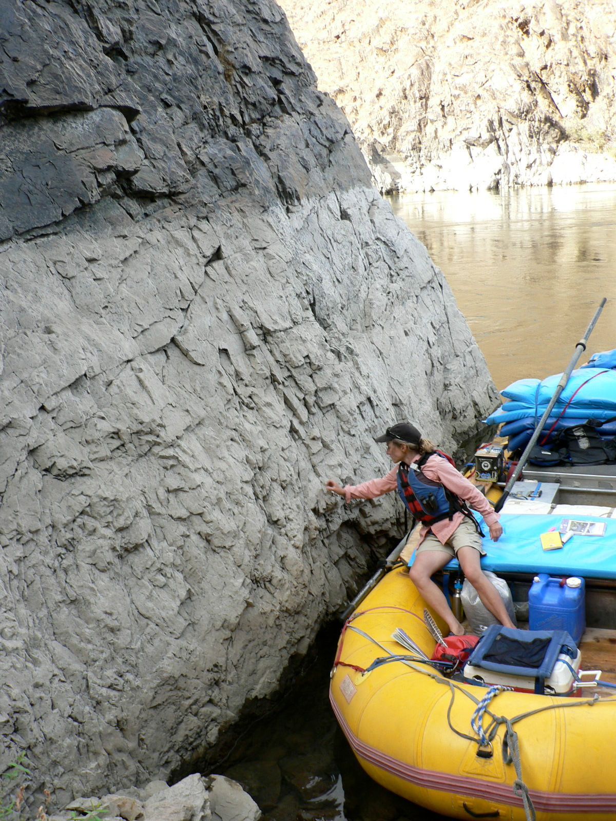 A man in a life jacket is sitting in a yellow raft next to a large rock.