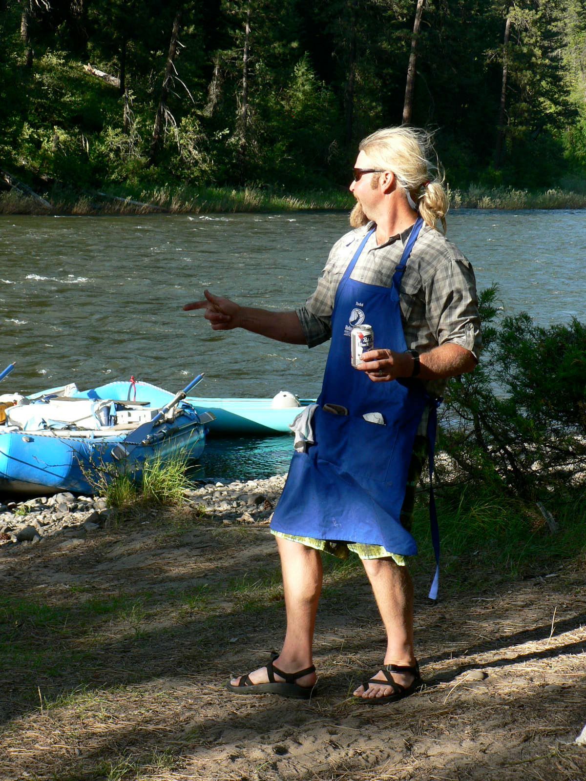 A man in a blue apron is standing next to a river