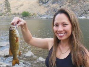 A woman is holding a fish in her hand and smiling.