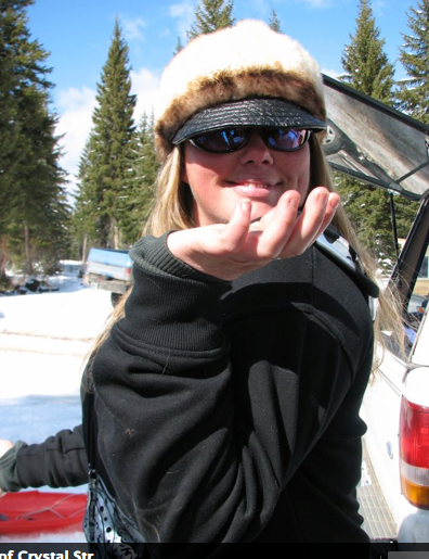 A woman wearing a fur hat and sunglasses holds up her hand