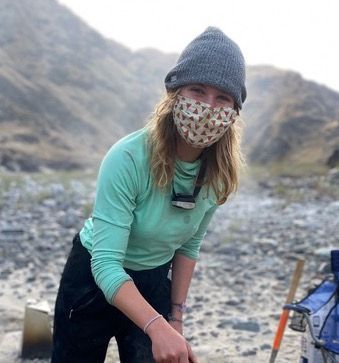 Woman Wearing a Mask and A Beanie Is Standing on A Rocky Beach