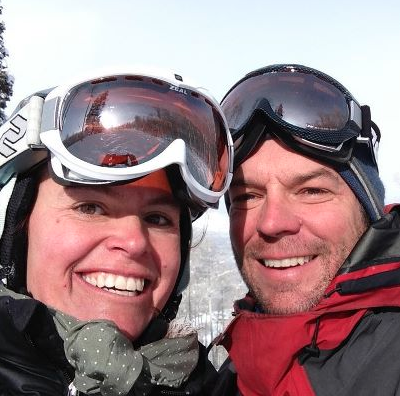 A man and a woman wearing ski goggles are smiling for the camera