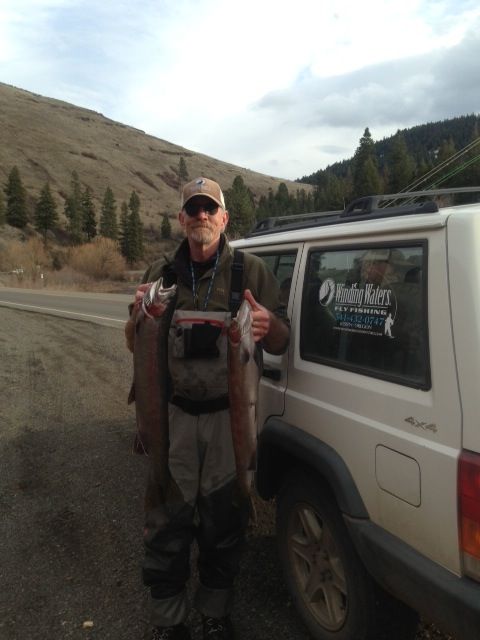 A man is holding two fish in front of a white jeep that says under armour