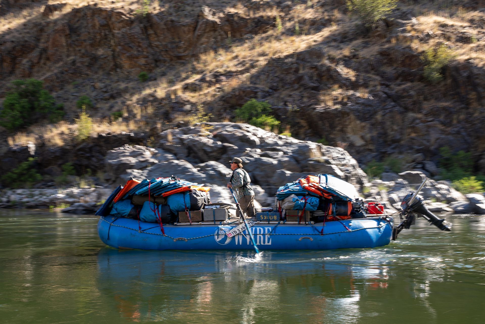 man standing on a blue large raft with rafting equipment on it