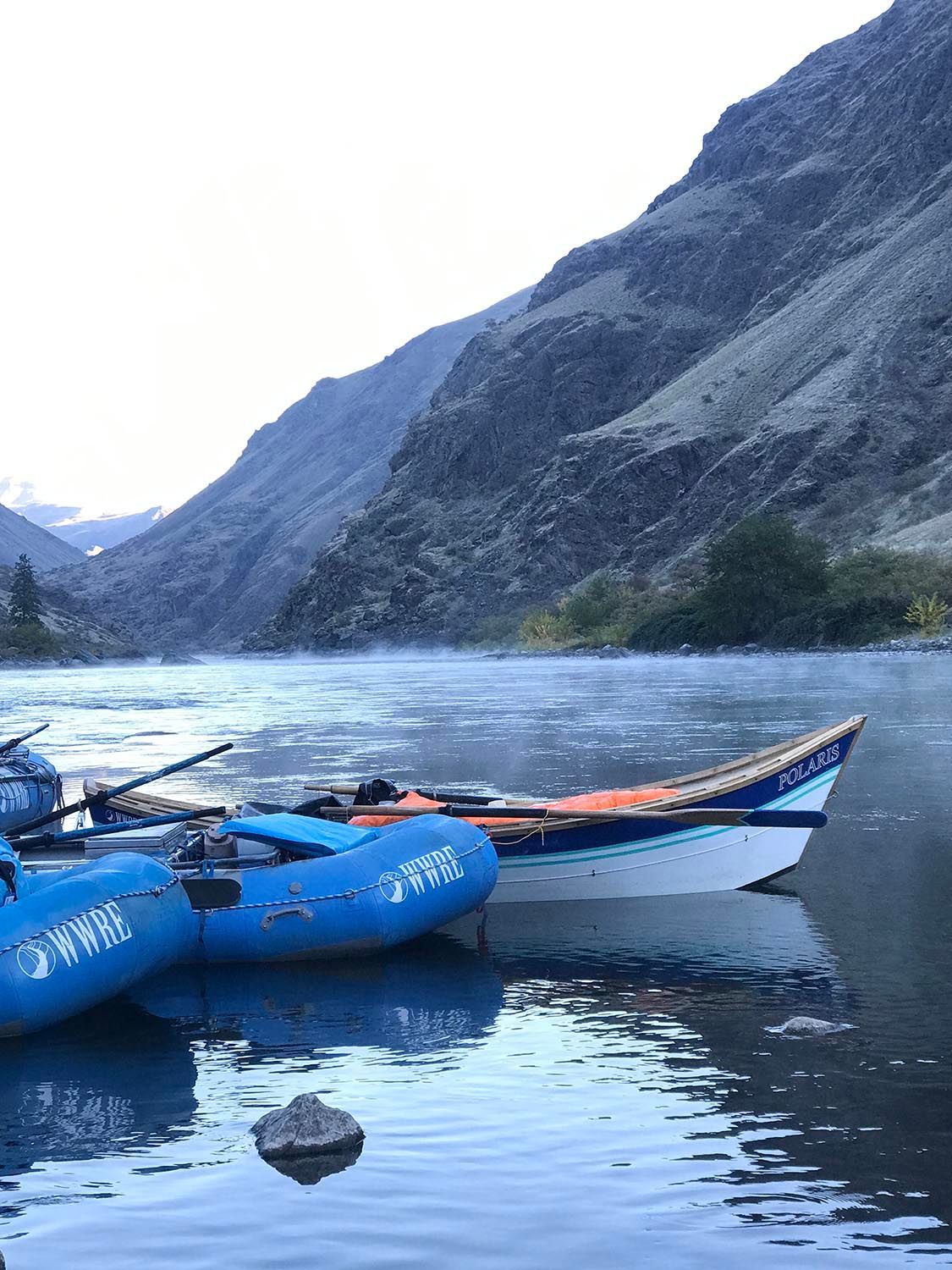 Two Rafts Are Docked on the Shore of A River with Mountains in The Background