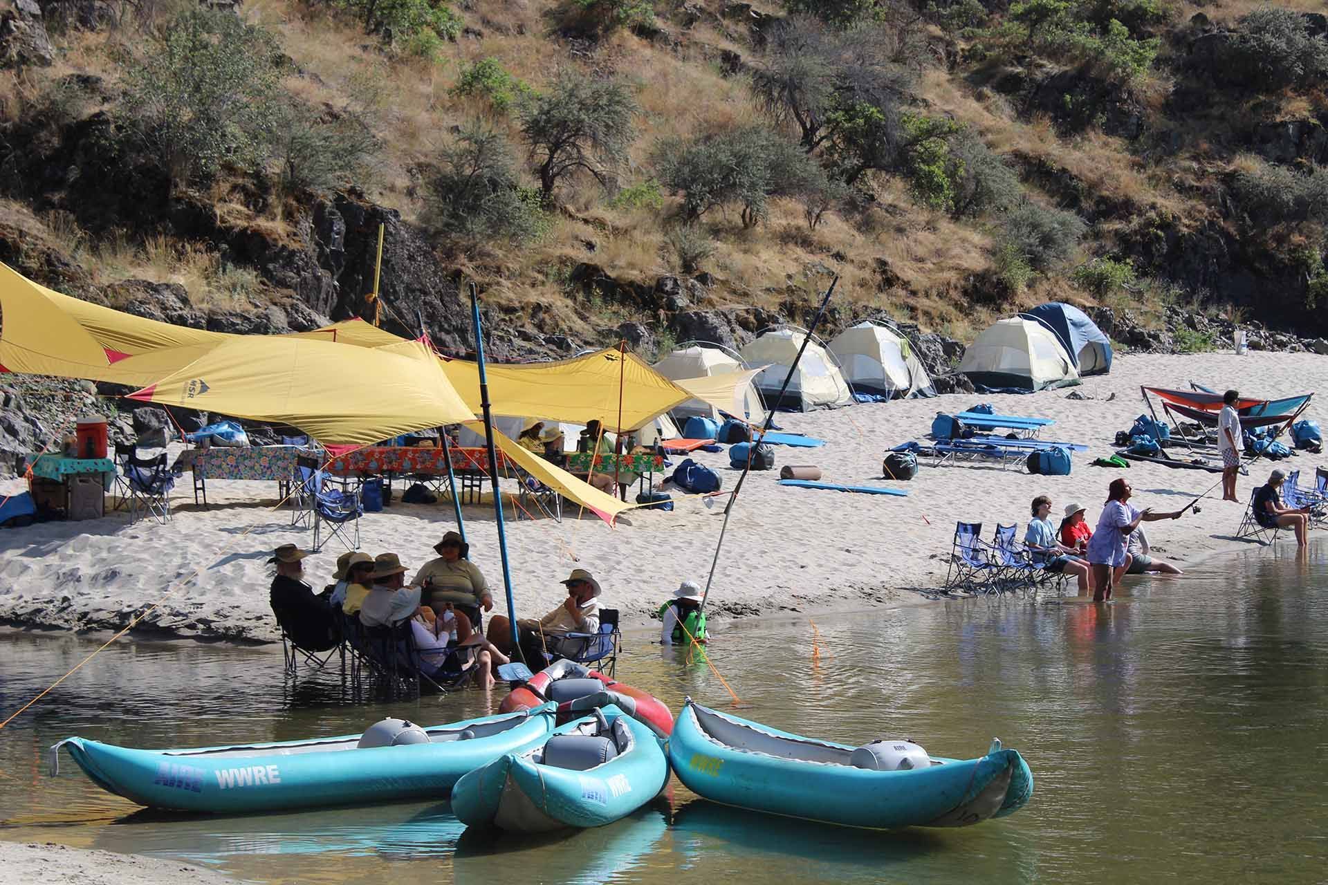 A group of people are sitting on a beach with kayaks and tents.