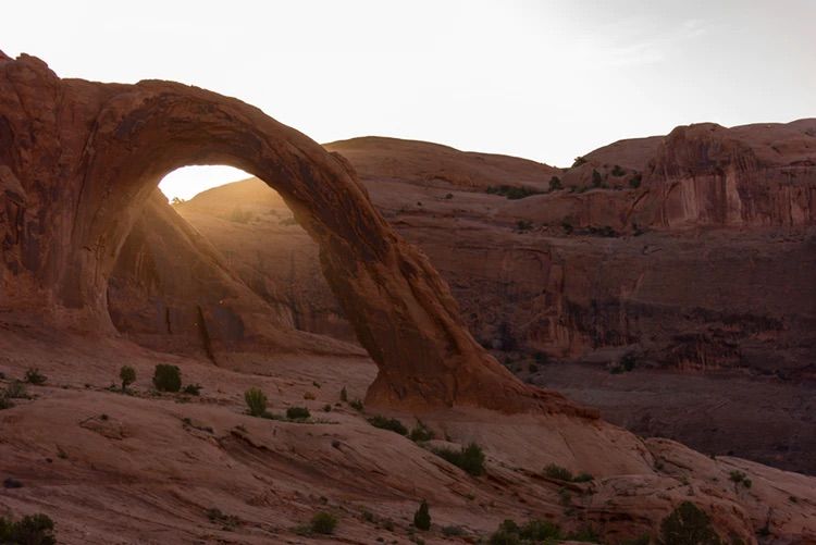 The sun is shining through the arch in the desert