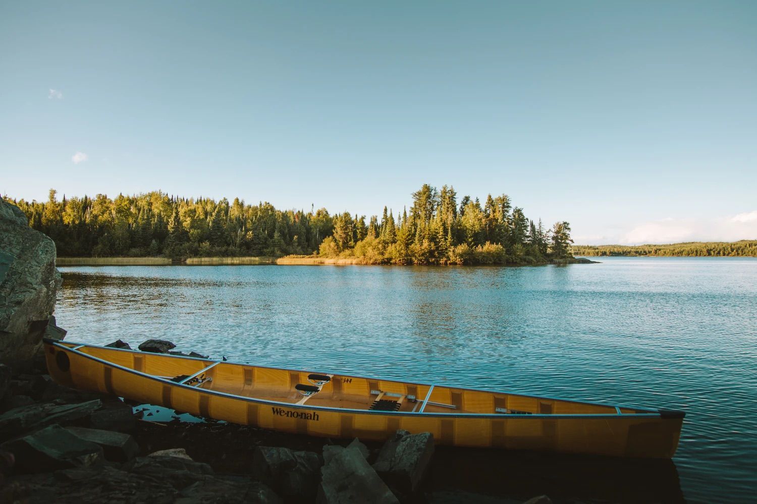 A yellow canoe is sitting on the shore of a lake.