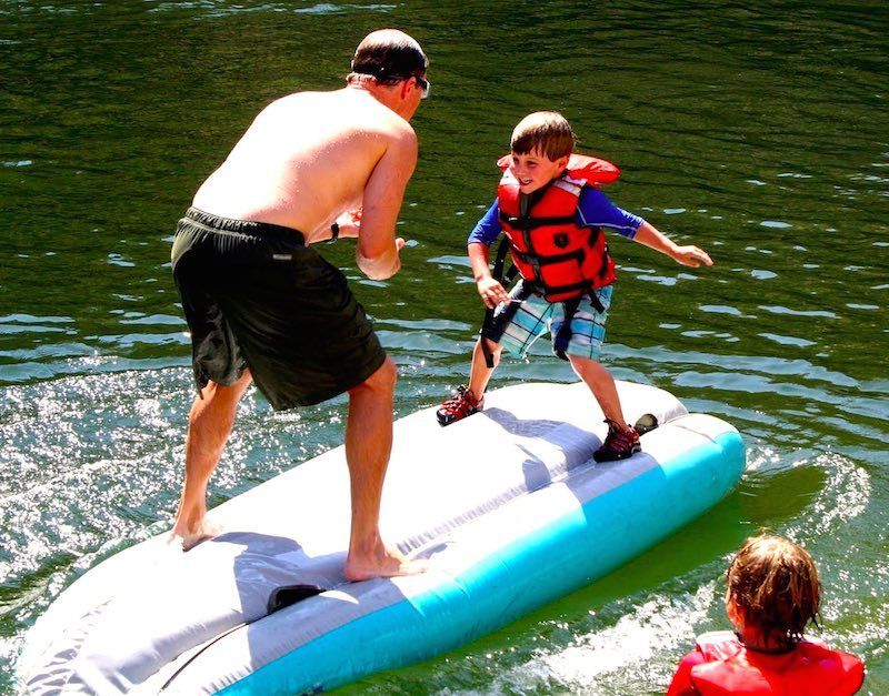 A boy in a life jacket is standing on a raft in the water