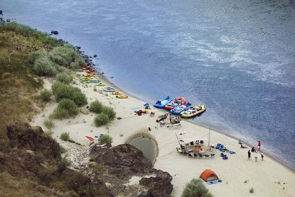 Group of People Are Sitting on A Sandy Beach Next to the River